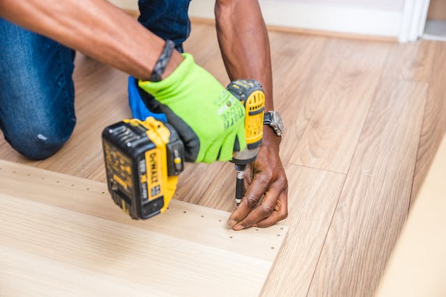 contractor wearing green work gloves and using an electric drill